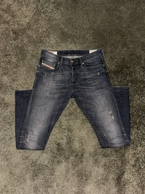 Mörkblå Diesel jeans - Säljer ett par mörkblå Diesel jeans med snygg tvätt och slitningar på benen. Klassisk femficksmodell med slim-fit passform och normal midja. Jeansen är gjorda i stretchigt denim för extra komfort och har Diesel-logga på fickan.