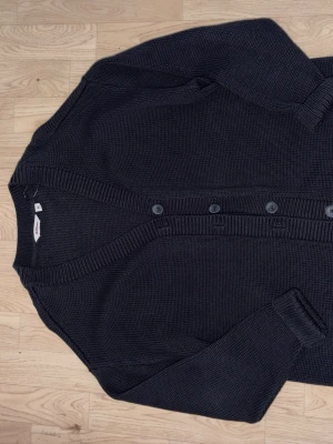 Mörkblå stickad kofta från Dobber - Säljer en mörkblå stickad kofta från Dobber i storlek M. Koftan har långa ärmar, ribbade muddar och knäppning med fyra knappar framtill. Perfekt för lager på lager och enkel att matcha med olika outfits.
