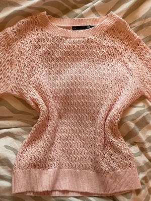 Rosa stickad tröja från 157 - Säljer en ljusrosa stickad tröja från 157 i storlek S. Tröjan har ett snyggt hålmönster och ribbade muddar vid hals, ärmslut och nederkant. Perfekt för vår och sommar, med korta ärmar och mjukt material som känns skönt mot huden.