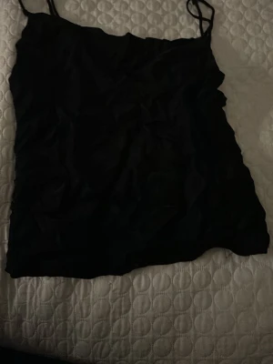 Svart linnetopp från Zara - Säljer en stilren svart linnetopp från Zara i storlek S. Toppen har tunna axelband och en enkel, rak passform som gör den lätt att matcha med olika outfits. Perfekt för varma dagar eller som lager under en jacka.