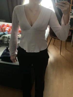 Ljusrosa knyttopp Gina - Supersöt ljusrosa omlottopp med v-ringning och långa ärmar. Toppen har knytband i midjan som ger en snygg passform och lätt volang nertill. Annvänd ett få tal gånger och har inga täcken på användning.