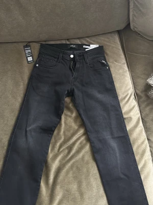 Replay Anbass svarta jeans, storlek 27/30 - Säljer ett par svarta Replay Anbass jeans med power stretch. Klassisk femficksmodell, silverfärgade detaljer och dragkedja. Snygg, smal passform och diskret Replay-logga på fickan. Perfekta för dig som gillar stilrena och bekväma jeans. Skulle säga att dem passar någon som är 170. Nypris 1200 kr. HELT NYA!