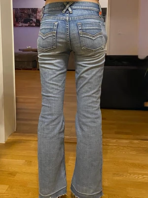 Blå bootcut jeans från Esprit - Säljer ett par ljusblå bootcut jeans med snygga detaljer som stora fickor fram med knappar och dekorativ söm bak. Jeansen har låg midja och rå, fransig kant längst ner på benen.Midjemått-35cm,lnnerbenslängd-75cm