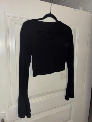 Svart croppad topp med trumpetärm Shein - En svart croppad topp från Shein med långa trumpetärmar och rund halsringning. Toppens material är mjukt och stretchigt, perfekt för att skapa en stilren och trendig look. Passar dig som gillar minimalistiska plagg med en twist.