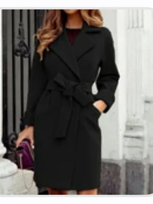 Svart kappa med bälte - Stilren svart kappa med knytbälte i midjan och klassisk krage. Jackan har långa ärmar och en rak passform som ger en snygg siluett. Perfekt för kyligare dagar och enkel att matcha med olika outfits.  Den är helt ny och oanvänd därav priset. Nypris:600kr!