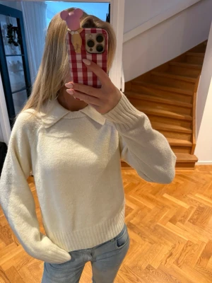 Vit  tröja med krage - Mysig vit stickad tröja med bred krage och långa ärmar. Tröjan har ribbade muddar vid ärmslut och nederkant, vilket ger en snygg och avslappnad look. Perfekt till jeans för en enkel men stilren outfit.