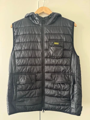 Svart dunväst från Barbour med luva - Inget slitage utöver lappen på insidan. Passar s/m.
