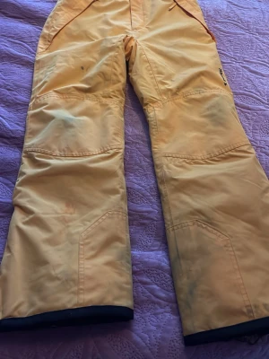 Gula täckbyxor från Everest stl 146 - Säljer ett par gula täckbyxor från Everest i storlek 146. Byxorna har förstärkta knän och benslut, justerbar midja och svart innerfoder. Perfekta för kalla dagar i backen eller snölek.