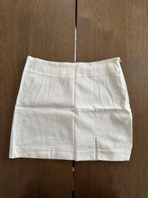 Vit kortkjol från Nelly - Vit kortkjol från NLY Trend i storlek XS. Kjolen har en rak passform, liten slits framtill och dragkedja i sidan. 