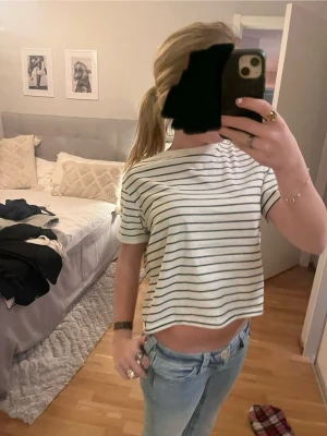 Vit croppad randig t-shirt - Säljer en vit croppad t-shirt med svarta horisontella ränder. T-shirten har korta ärmar och en avslappnad passform som sitter snyggt på kroppen. Perfekt för dig som gillar en enkel och fräsch stil med lite edge.