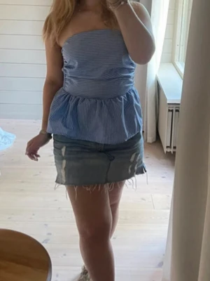 Blåvit randig bandeau tubtopp - Säljer en blåvit randig bandeau tubtopp med volang nedtill. Toppen är axelbandslös och har en söt, luftig passform som passar perfekt till sommaren. 