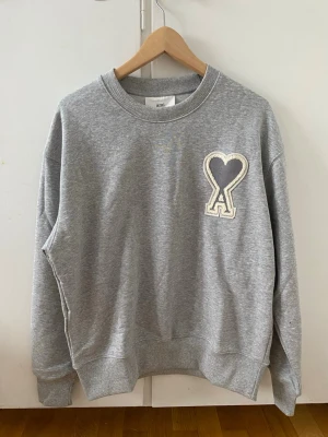 Grå sweatshirt från Ami Paris - Storlek: M Skick: Ny & oanvänd  Grå Ami Paris sweatshirt i premiumkvalitet med ikonisk broderad hjärtlogga framtill. Bekväm och stilren modell med klassisk crewneck och ribbade avslut. Perfekt vardagströja med lyxkänsla.