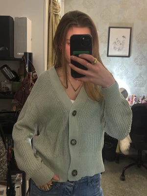 Ljusgrön stickad kofta med stora knappar - Superfin ljusgrön stickad kofta med stora, mörka knappar framtill. Koftan har v-ringning, lång ärm och ribbade muddar samt nederkant🥰