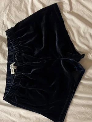 Mörkblå sammets-shorts  - Säljer ett par mörkblå shorts i mjuk och glansig sammet. De har elastisk midja och en klassisk, enkel design utan extra detaljer. Perfekta för dig som gillar en chill och stilren look.