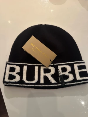 Burberry mössa  - Bilden visar en svart mössa från Burberry med vit logotyp, inte en väst. Kan ej ge västbeskrivning.