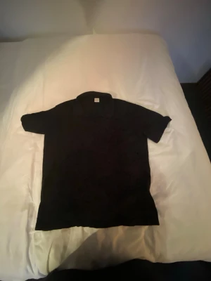 Marinblå piké t-shirt från Lindex Kids - En marinblå piké t-shirt från Lindex Kids i storlek 146/152. Ingen krage och korta ärmar, perfekt för en clean och enkel stil. Tillverkad i mjuk bomull som känns skön mot huden.