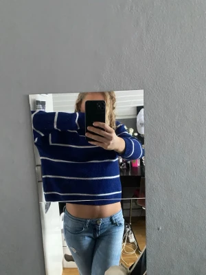 Blå randig stickad tröja - Mysig blå stickad tröja med vita horisontella ränder. Tröjan har en lite croppad passform och långa ärmar. Perfekt för dig som gillar en avslappnad och trendig stil. Passar bra till jeans eller kjol. 