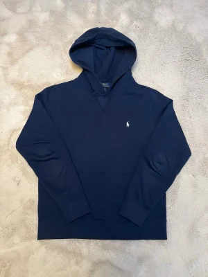 Ralph lauren hoodie  - Klassisk hoodie från Polo Ralph Lauren i marinblått med vit logga. Mycket fint skick och sparsamt använd. Storlek 14–16, motsvarar ungefär XS. Hög kvalitet i en klassisk och lättmatchad design. Nypris ca 1 300 kr och självklart 100 % äkta. Säljs då den inte kommer till användning längre.