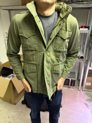 Grön fieldjacket  - Säljer en grön parkajacka från The Gallerist med två unika patches på ärmarna. Jackan har fyra stora fickor framtill, snörning i midjan och klassisk krage. Materialet är bomull.