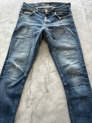 Blå Nudie Jeans, storlek 31/32 - Säljer mina nudie jeans då de har blivit lite små för mig. Riktigt sköna slitningar men inga hål. Modellen är Grim Tim, Authentic Deep med 99% bomull och 1% elastan. Nypris 1600kr Skriv gärna om ni har fler frågor :)