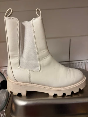 Vita chunky chelsea boots - Säljer ett par vita chelsea boots med chunky sula och elastiska paneler på sidorna. Skorna har rund tå och är tillverkade i slätt syntetmaterial. Perfekta för dig som vill ha en stilren men edgy look.