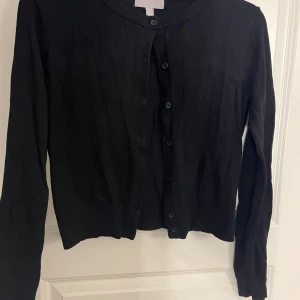 Svart kofta från H&M med knappar - En klassisk svart kofta från H&M med rund halsringning och knäppning framtill. 