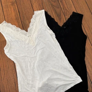 2-pack linne med spetskant svart & vit - Två snygga linnetoppar i svart och vitt med v-ringad spetskant framtill. Båda är ärmlösa och har en feminin touch med blommig spets längs urringningen. Perfekta att styla lager på lager eller som de är. Kan köpa en av dom eller båda❤️❤️