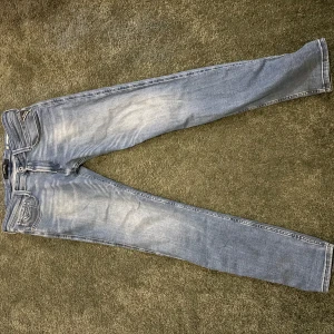 Replay Anbass ljusblå jeans - Säljer ett par Replay Anbass jeans i ljusblå tvätt med snygga slitningar. Modellen har klassisk femficksdesign, smal passform och raka ben. Jeansen är tillverkade i mjukt denimtyg som sitter skönt hela dagen. Perfekta för dig som gillar stilrena och moderna jeans.