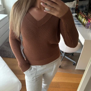 Brun stickad v-ringad tröja - Säljer en brun stickad tröja med v-ringning och lång ärm. Tröjan har en snygg ribbad kant vid halsen och ärmarna, och är i en loose fit som är både chill och trendig. Perfekt för lager-på-lager under höst och vinter.