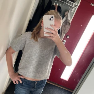 Grå croppad t-shirt i ull - Säljer en enkel och stilren grå stickad t-shirt med korta ärmar. T-shirten är stickad i mjuk ull och har en rund halsringning. Perfekt för dig som gillar en chill och clean look.