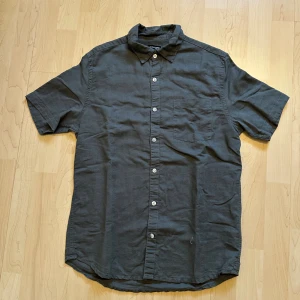 Mörkgrön kortärmad skjorta - Snygg mörkgrön skjorta med korta ärmar och klassisk krage. Skjortan har knappar framtill och en bröstficka. Perfekt för en avslappnad och stilren look.