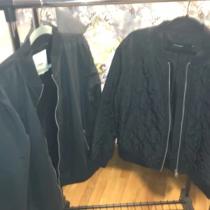 Svarta bomberjackor från Vero Moda & Produkt - Två svarta bomberjackor, en från Vero Moda med quiltad yta och en från Produkt med slät finish. Båda har dragkedja framtill, ribbade muddar och klassisk bomberkrage. Perfekta för dig som gillar stilren och enkel streetwear.en xl och en L