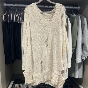 Oversized offwhite stickad tröja - En oversized stickad tröja i v-ringning och sliten look. Tröjan har flera hål och slitningar för en edgy vibe, samt breda ribbade muddar vid ärmslut och nederkant. Passar allt från XS-M beroende hör man önskar passformen. Passar snyggt till jeans el som ”kortklänning” 👌🏼 Skitsnygg!