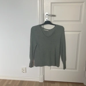 Grå ribbad stickad tröja från ONLY - Mysig grå stickad tröja från ONLY i storlek S. Tröjan har v-ringning, långärmade ärmar och är ribbstickad för en snygg och enkel look. Perfekt att matcha med jeans eller kjol för en chill stil.