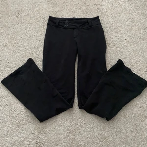 Svarta kostymbyxor - Svarta bootcut kostymbyxor från Gina Tricot med två knappar i midjan och bälteshällor. Byxorna har en klassisk bootcut-modell med utsvängda ben, låg midja och är tillverkade i ett mjukt bomullsmaterial. Passar dig som är 158 cm lång och neråt. Perfekta för en stilren och trendig look.