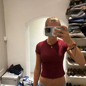 Vinröd tajt topp med kort ärm - Säljer en vinröd croppad topp med korta ärmar och rund hals. Toppen har en slim passform och är tillverkad i mjuk bomull, perfekt för att styla med jeans eller kjol. Enkel och stilren design som ger en snygg siluett.