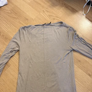 Beige långärmad topp XS - En enkel och stilren beige långärmad topp i mjukt och tunt material. Perfekt att matcha med jeans eller kjol för en clean look. Modellen är rak och har en klassisk rund halsringning.