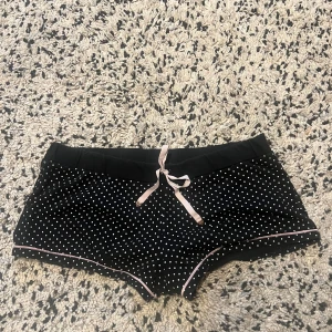 Svarta prickiga shorts med snörning - Snygga svarta shorts med ljusrosa prickar och ljusrosa snörning i midjan🩷. De har en loose passform och är dekorerade med rosa kantband längs benen. Perfekta för varma kvällar hemma eller som pyjamasshorts. Mjukt bomullsmaterial som känns skönt mot huden☺️.