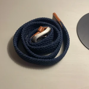 Blått flätat bälte från Jack & Jones - Snyggt blått flätat bälte från Jack & Jones med detaljer i brunt skinn och ett silvrigt spänne. Perfekt accessoar för att lyfta din outfit med en stilren och modern touch. Bältet har en klassisk design med en twist tack vare det flätade materialet.