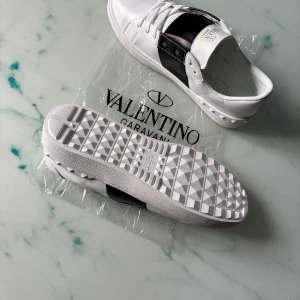 Open sneaker  -  sneakers i vitt skinn med bred svart läderdetalj över mitten. Klassisk rund tå, snörning och coola nitar på hälen. Tjock, mönstrad sula för extra edge. Perfekta för dig som vill sticka ut med lyxig Grisch stil.