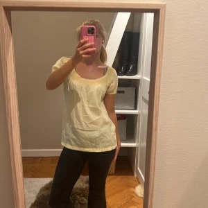 Ljusgul blus  - Säljer en söt ljusgul blus med rundad, smockad halsringning. Blusen har en luftig passform och är perfekt för varma dagar. Materialet känns lätt och skönt mot huden. Superfin att styla med jeans eller kjol för en fräsch look.