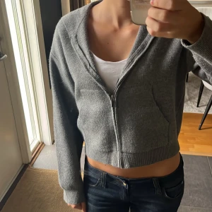 Grå croppad hoodie från Zara - Grå croppad hoodie från Zara med dragkedja framtill och huva. Tröjan är stickad och har långa ärmar samt ribbade muddar vid ärmslut och nederkant. Väldigt tjockts och fint material och använt bara 2 gånger! Står på tröjan storlek 164 men passar mig som vanligtvis har S!