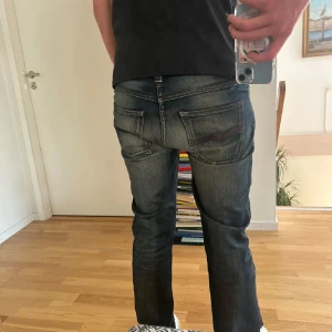 Nudie mörkblå jeans slim fit - Säljer ett par mörkblå jeans från nudie med snyggt slitna detaljer och klassiska bakfickor med broderad logga. Jeansen har slim passform och normal midja, tillverkade i mjukt denimtyg som sitter skönt hela dagen. Säljer eftersom jag har växt ut dom. Priset är inte hackat i sten!