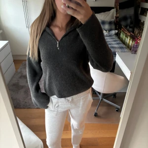 Mörkgrå stickad half zip tröja - Mysig mörkgrå stickad tröja med half zip-dragkedja i halsen. Tröjan har en ribbad struktur och långa ärmar, perfekt för lager-på-lager och chill dagar. Snygg och enkel att matcha med både jeans och mjukisbyxor.