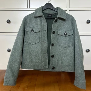 Grön  kappa från Vero Moda i XS  - Hej, jag säljer en kort kappa  från Vero Moda. Kappan är ljus grön och har klassisk krage, stora bröstfickor med knappar och raka ärmar. Perfekt lager-på-lager-plagg med stilren look och rejäla knappar framtill. Super snygg nu till hösten 💕