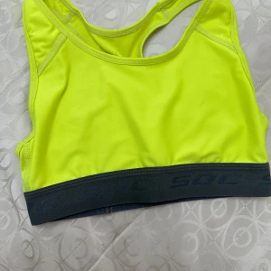 Neongul sporttopp från SOC - Sportig neongul linnetopp från SOC med grå resårkant och brottarrygg. Perfekt för träning och har TCS Air-detalj på ryggen. Sitter tight och är tillverkad i ett syntetmaterial som andas.