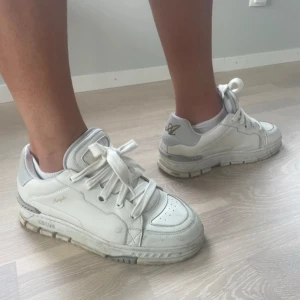 Vita sneakers från Axel Arigato - Snygga vita sneakers från Axel Arigato med chunky sula och gulddetaljer på hälen. Skorna har breda vita snören, perforerad tå och logga på sidan och baksidan. 