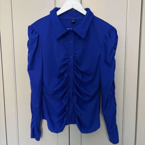 Blå skjorta från SHEIN - Blå skjorta från SHEIN i storlek L och snygga rynkade detaljer framtill och längs ärmarna. Skjortan har klassisk krage och knappar. 