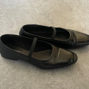 Svarta ballerinaskor från Vagabond - Klassiska svarta ballerinaskor från Vagabond i skinn med elastiskt band över foten. Snygg, minimalistisk design med rund tå och platt sula. Perfekta för en stilren look och funkar till många outfits.