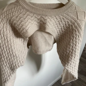Beige croppad stickad tröja H&M - Säljer en beige croppad stickad tröja från H&M i storlek S. Tröjan har ett snyggt flätstickat mönster framtill och längs ärmarna, ribbad halsringning och långa ärmar. Perfekt för lager-på-lager och chill höst- eller vinterstil.